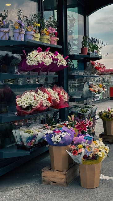 An outdoor floral display at leytonflorist.co.uk showcasing a variety of fresh flower arrangements and bouquets arranged on metal shelves and wooden crates. The flowers include pink, white, purple, an